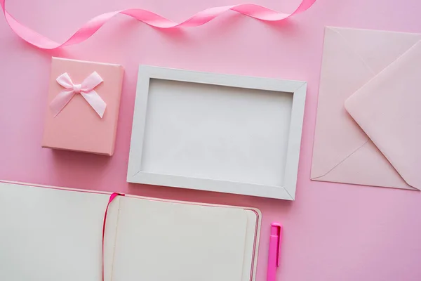 Vista dall'alto del quaderno bianco vicino a cornice, busta e confezione regalo su rosa — Stock Photo