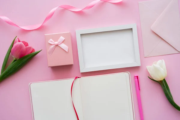 Draufsicht auf Tulpen in Rahmennähe, Umschlag, leeres Notizbuch und Geschenkbox auf rosa — Stockfoto