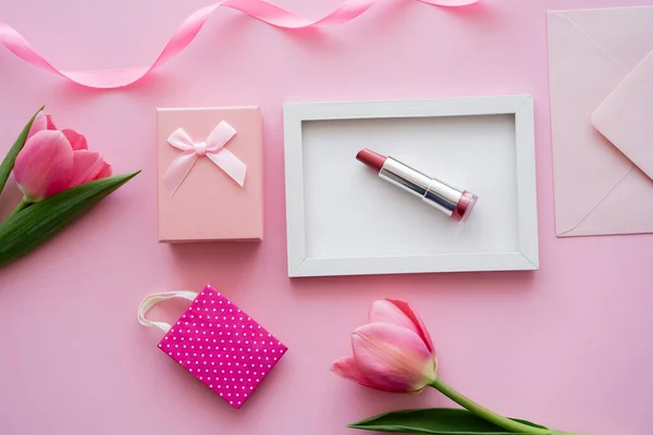Вид зверху на тюльпани біля рамки з помадою, конвертом та подарунковою коробкою на рожевому — стокове фото
