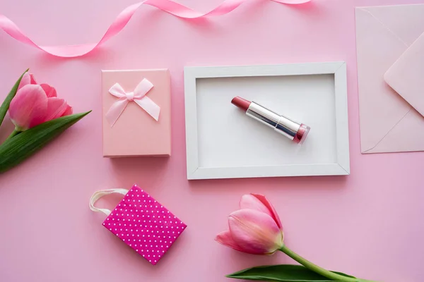 Vista superior de tulipanes cerca del marco con lápiz labial, sobre y caja de regalo en rosa - foto de stock