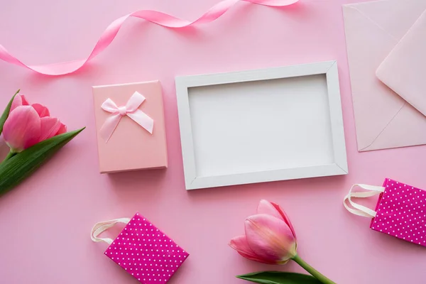 Vista dall'alto di tulipani vicino cornice, borse della spesa, busta e confezione regalo su rosa — Foto stock