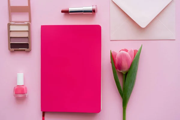 Vista superior del tulipán cerca del cuaderno, sobre y cosméticos decorativos en rosa - foto de stock