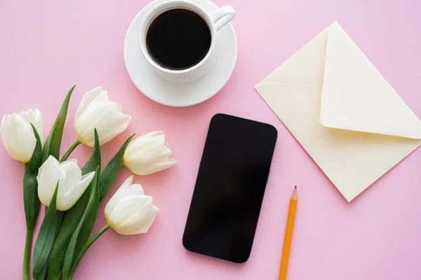 Vista superior de tulipanes blancos cerca de smartphone con pantalla en blanco y taza de café en rosa - foto de stock