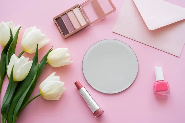 Draufsicht auf weiße Tulpen in der Nähe von Umschlag und dekorativer Kosmetik auf rosa — Stockfoto