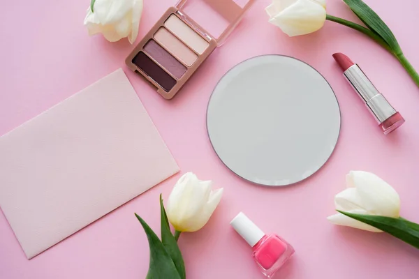 Верхний вид белых тюльпанов рядом с зеркалом, конверт и декоративная косметика на розовый — стоковое фото