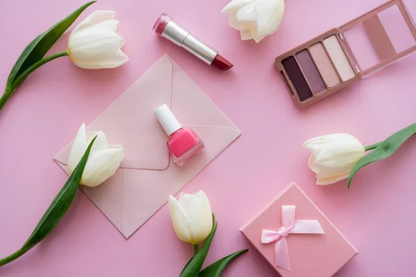 Vista superior de tulipas brancas perto do envelope, caixa de presente e cosméticos decorativos em rosa — Fotografia de Stock