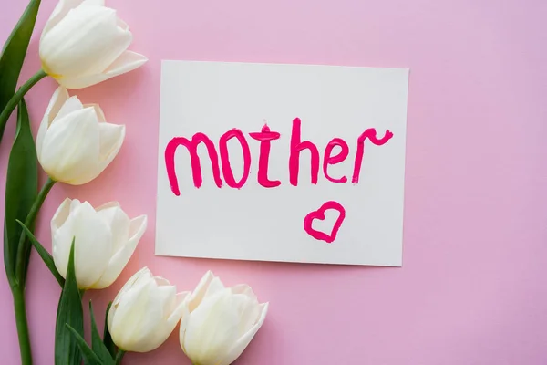 Top view of white tulips near greeting card with mother lettering on pink — Stock Photo