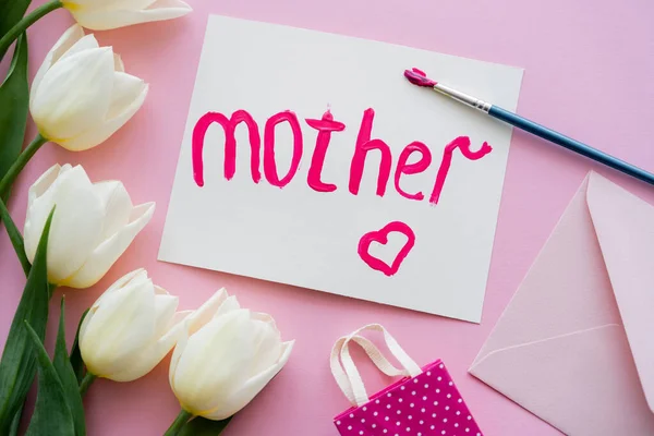 Top view of paintbrush with paint near card with mother lettering and white flowers on pink — Stock Photo