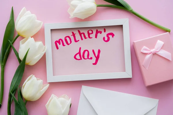 Top view of card with mothers day lettering in frame near gift box, envelope and white flowers on pink — Stock Photo