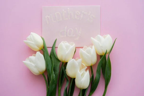 Vista dall'alto di busta con scritte di giorno di madri vicino a fiori bianchi su rosa — Foto stock