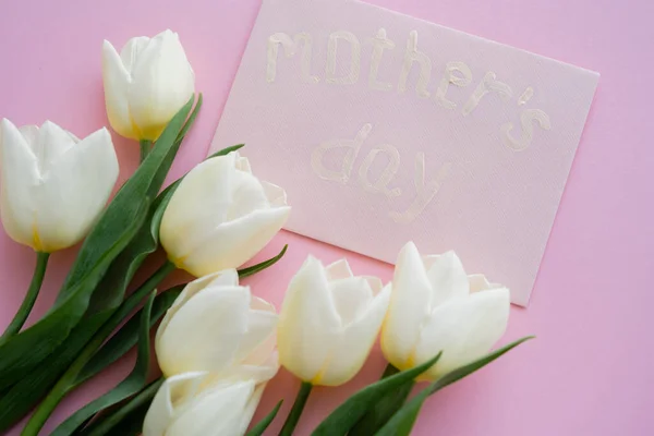 Vue du dessus de l'enveloppe avec des lettres de la fête des mères près de fleurs en fleurs sur rose — Photo de stock