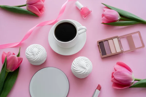 Top view of cup with coffee near zephyr, decorative cosmetics and tulips on pink — Stock Photo