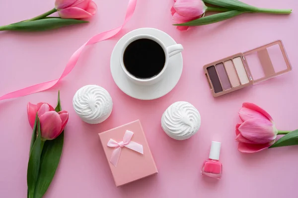 Вид зверху на зефір, декоративна косметика і тюльпани біля чашки кави на рожевому — стокове фото