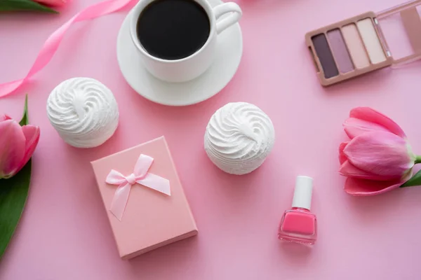 Top view of gift box, zephyr, decorative cosmetics and tulips near cup of coffee on pink — Stock Photo