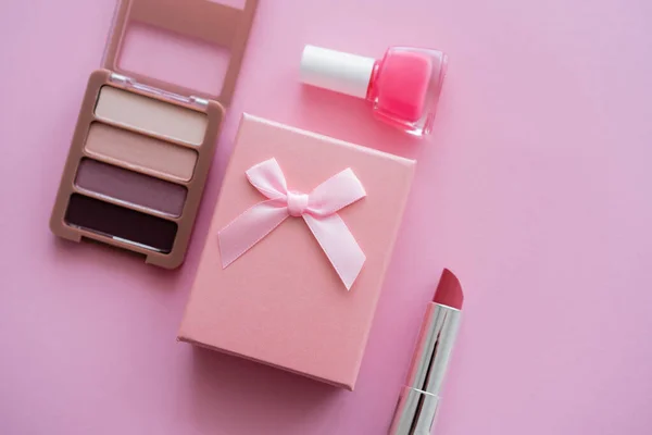 Vista dall'alto della confezione regalo con fiocco vicino a cosmetici decorativi su rosa — Foto stock