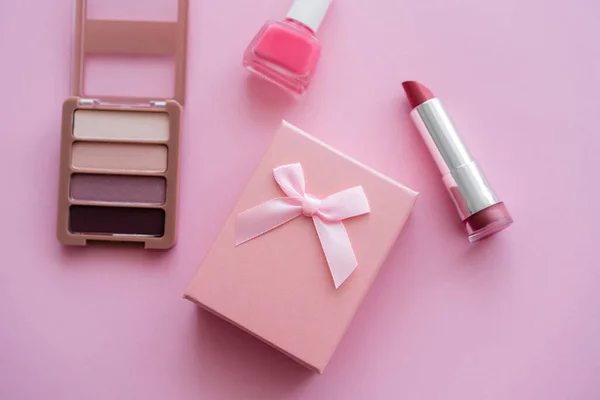 Top view of present with bow near decorative cosmetics on pink — Stock Photo