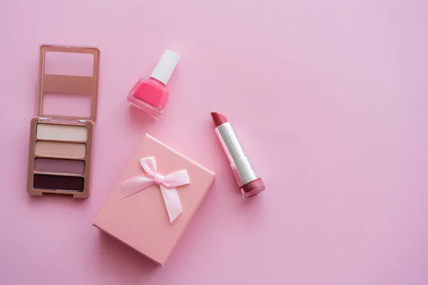 Top view of decorative cosmetics near present with bow on pink — Stock Photo