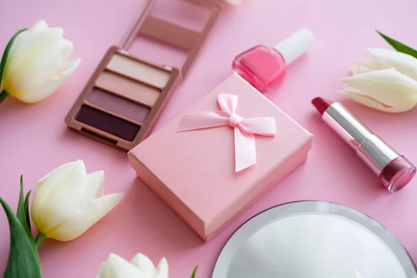 Закрытие белых цветов, подарочной коробки и декоративной косметики на розовый — стоковое фото