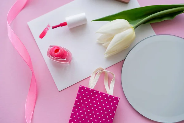 Вид зверху на пензлик на листівці біля лаку для нігтів, білий тюльпан і сумка для покупок на рожевому — стокове фото