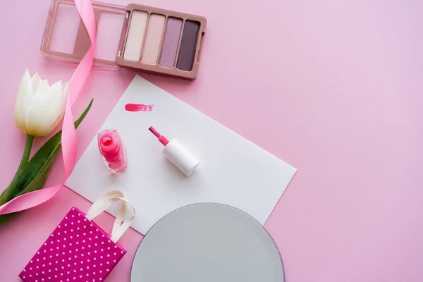 Pinselstrich auf Karte in der Nähe von Nagellack, weißer Tulpe, Lidschatten und Einkaufstasche auf rosa — Stockfoto