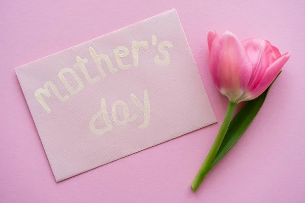 Vue du dessus de la tulipe près de l'enveloppe avec lettrage de la fête des mères sur rose — Photo de stock