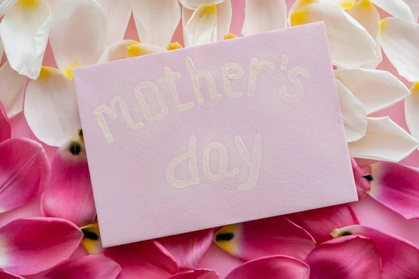 Vue du dessus de l'enveloppe avec inscription de la fête des mères sur des pétales floraux blancs et roses — Photo de stock