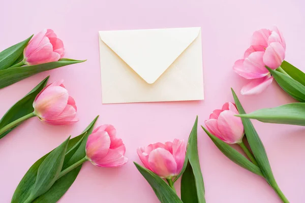 Flache Lage blühender Tulpen mit grünen Blättern in der Nähe von Hülle auf rosa, Muttertagskonzept — Stockfoto