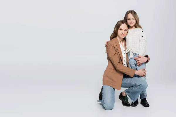 Frau blickt in die Kamera, während sie Tochter auf grauem Hintergrund umarmt — Stockfoto