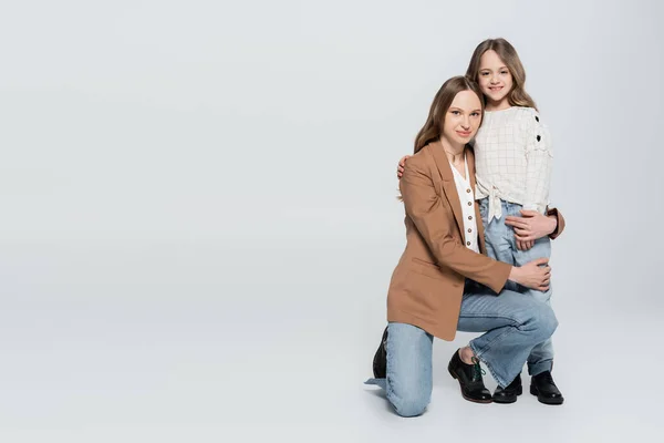 Woman looking at camera while hugging daughter on grey background — Stock Photo