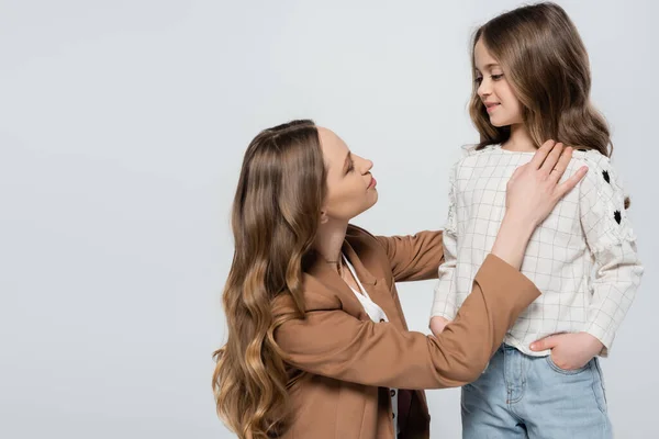 Woman with long hair looking at daughter standing with hand in pocket isolated on grey — Stock Photo