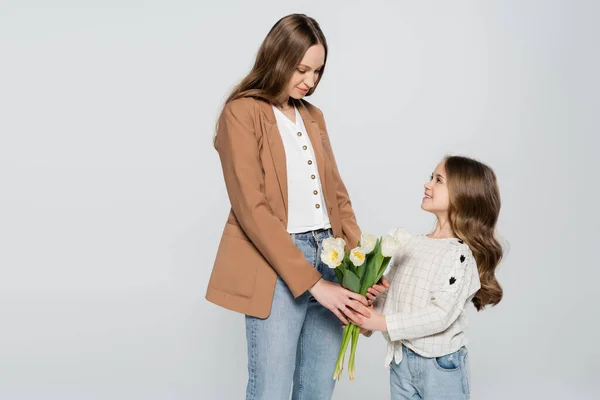 Lächelndes Mädchen präsentiert Tulpen an Mutter isoliert auf grau — Stockfoto