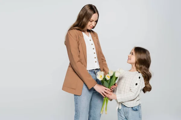 Smiling girl presenting tulips to mother isolated on grey — Stock Photo