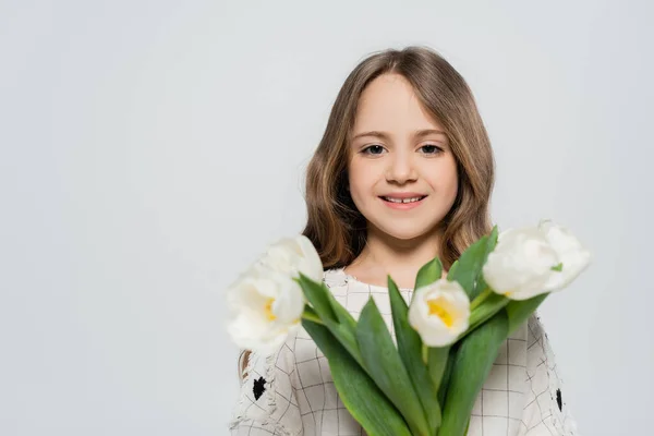 Ragazza positiva con bouquet sfocato di tulipani bianchi guardando la fotocamera isolata sul grigio — Foto stock