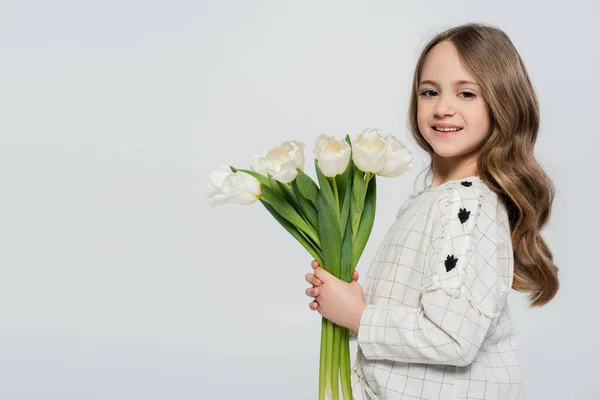 Glückliches Mädchen mit langen Haaren, das einen Strauß Tulpen in die Kamera hält und isoliert auf grau blickt — Stockfoto