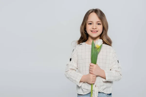 Fille aux cheveux longs tenant tulipe blanche et souriant à la caméra isolé sur gris — Photo de stock