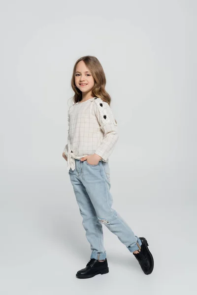 Visão de comprimento total da menina posando com as mãos em bolsos de jeans no fundo cinza — Fotografia de Stock