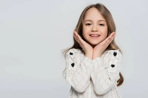 Cheerful girl smiling at camera while holding hands near face isolated on grey — Stock Photo