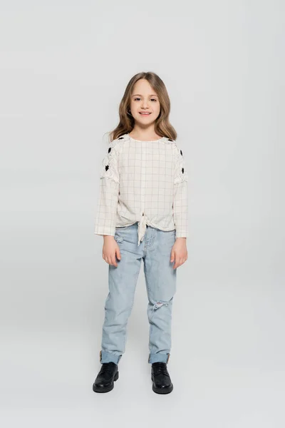 Ganzkörperansicht des lächelnden Mädchens in Jeans und weißer Bluse auf grauem Hintergrund — Stockfoto