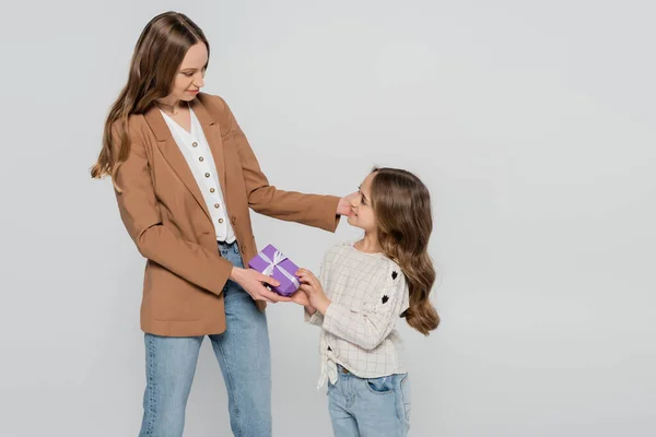 Sorridente ragazza che presenta il regalo di giorno delle madri alla mamma isolata sul grigio — Foto stock