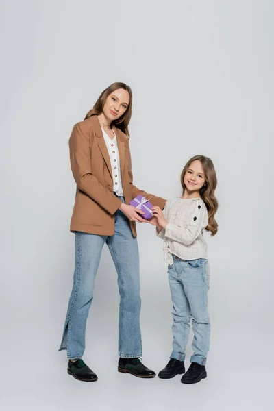 Full length view of trendy mother and daughter smiling near gift box on grey background — Stock Photo