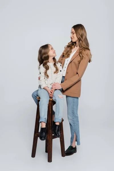 Femme heureuse et élégante près de fille assise sur un tabouret haut sur fond gris — Photo de stock