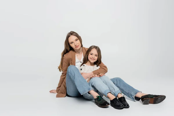 Vue pleine longueur de la mère et de l'enfant dans des vêtements à la mode assis sur fond gris — Photo de stock