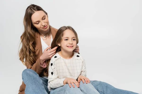 Woman braiding long hair of cheerful daughter isolated on grey — Stock Photo