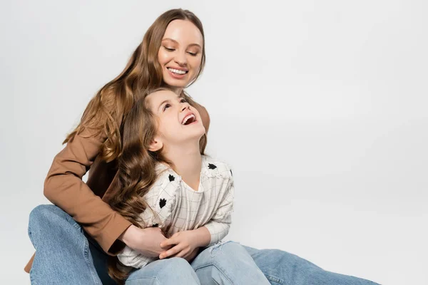 Happy woman embracing laughing daughter isolated on grey — Stock Photo