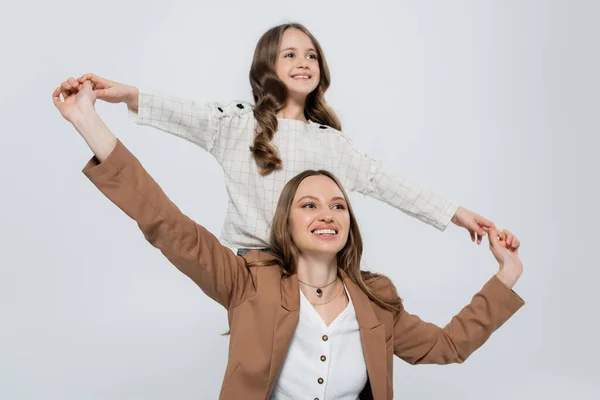 Madre sorridente e bambino che si tiene per mano e distoglie lo sguardo isolato sul grigio — Foto stock