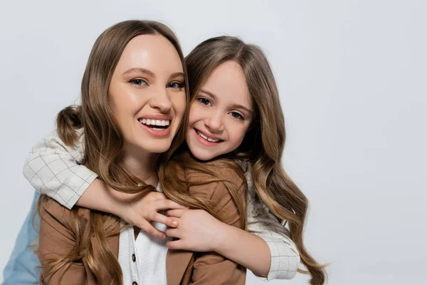 Zufriedenes Mädchen umarmt fröhliche Mutter und blickt isoliert in die Kamera auf grau — Stockfoto