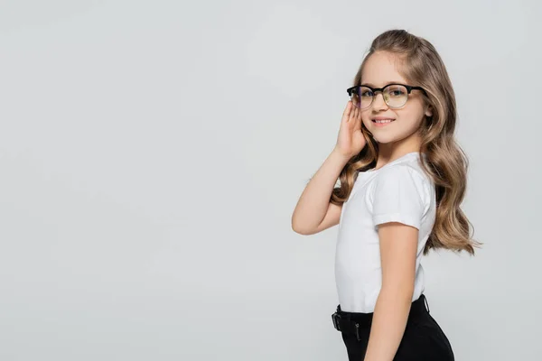 Niña sonriente en camiseta blanca ajustando gafas aisladas en gris - foto de stock