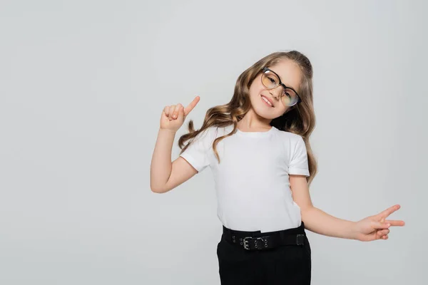 Glückliches Mädchen mit Brille, das Siegeszeichen zeigt und mit dem Finger isoliert auf grau zeigt — Stockfoto