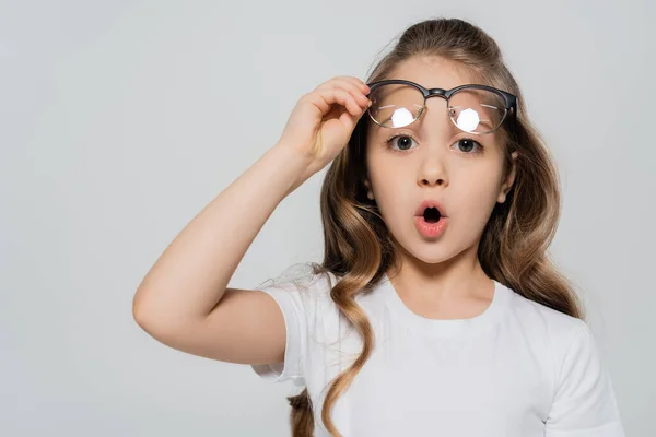 Surprised girl with open mouth holding eyeglasses and looking at camera isolated on grey — Stock Photo