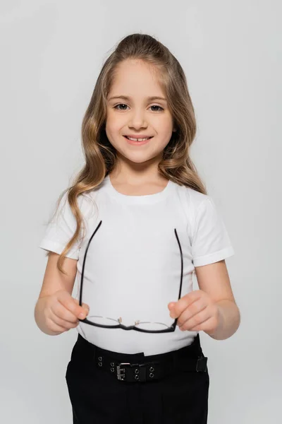 Fröhliches Mädchen im weißen T-Shirt mit Brille und Blick in die Kamera vereinzelt auf grau — Stockfoto